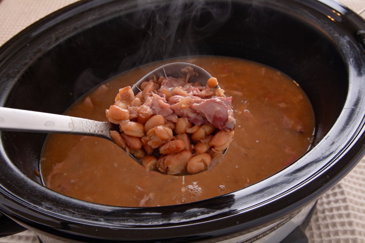 A ladele scooping up finished pinto beans from a crockpot.