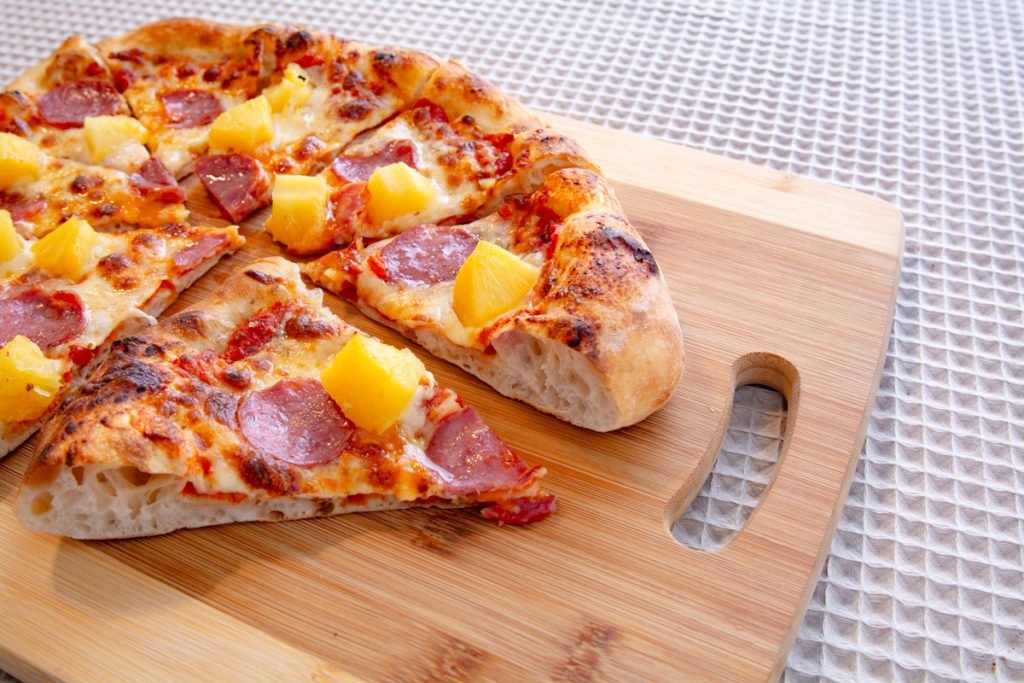 pepperoni and pineapple pizza on a cutting board. The pizza is cut to show the air pockets in the crust
